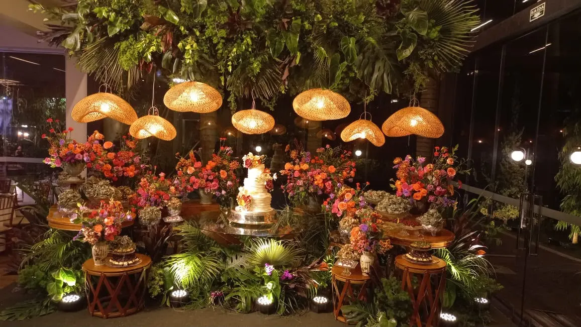 Mesa do bolo de casamento com flores laranja e luminárias de palha